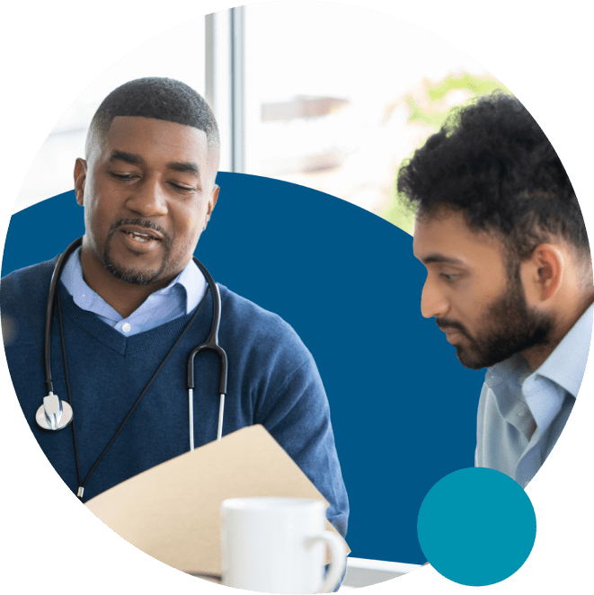 A healthcare professional with a stethoscope talks to a man while holding a folder. They appear to be discussing something important. Both are casually dressed, and the setting suggests an office or consultation room.